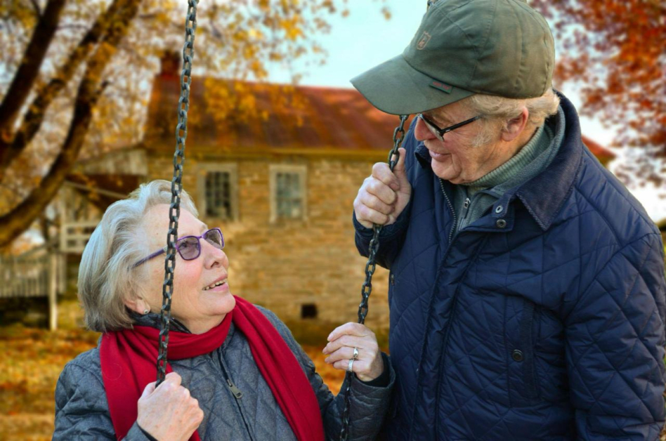 An elderly couple shares a warm moment together outdoors surrounded by autumn foliage.