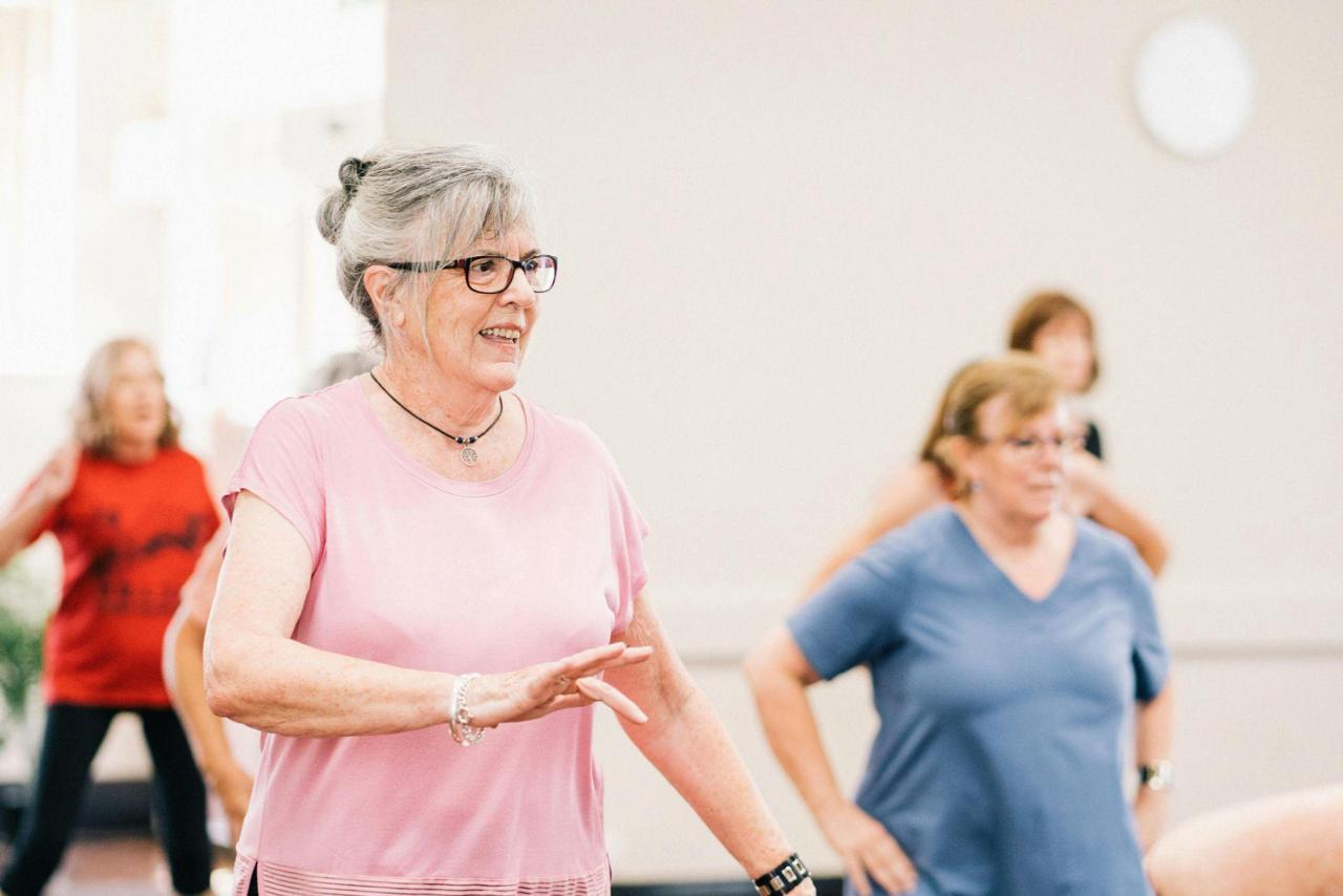 A group of senior women participate in a fitness class together in a bright, open room.